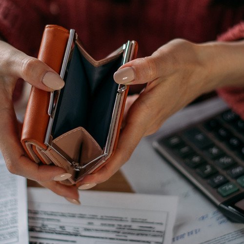 Eine Frau h&auml;lt eine leere Geldb&ouml;rse in die Kamera, auf dem Tisch liegen Taschenrechner und Stromrechnungen. Symbolfoto: Adobe Stock