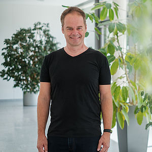 Prof. Dr. Ralf Hohlfeld steht in schwarzem T-Shirt auf einem Gang der Universität.