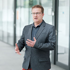 Prof. Dr.-Ing. Christian Hammer, Inhaber des Lehrstuhls für Software Engineering I, steht argumentierend auf einem Flur. 