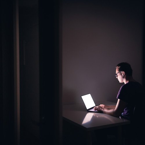 Symbolbild: Crowdworker. Eine Person sitzt in einem dunklen Zimmer allein vor dem Laptop.
