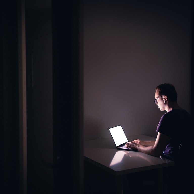 Symbolbild: Crowdworker. Eine Person sitzt in einem dunklen Zimmer allein vor dem Laptop.