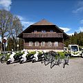 Elektrofahrzeuge vor einem alten Holzhaus im Böhmerwald. Foto: e-Sumava