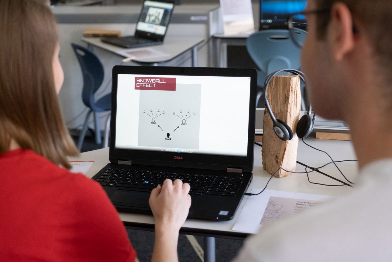 Zwei Studierende sitzen vor einem Laptop und sehen sich ein Video zur technischen Seite von Fake-News an.