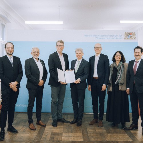 Sechs Herren und eine Dame &uuml;berreichen eine Kooperationsvereinbarung zur Gr&uuml;ndung des Zentrums Hochschule und Nachhaltigkeit Bayern (BayZeN) im Bayerischen Staatsministerium f&uuml;r Wissenschaft und Kunst: von links nach rechts sieht man Prof. Dr. Harald Kosch von der Universit&auml;t Passau, Dr. Eric Veulliet von der HSWT, Wissenschaftsminister Markus Blume, Prof. Dr. Clemens Bulitta von der OTHAW, Prof. Dr. Niels Oberbeck von der Ohm, Prof. Dr. Gabriele Gien von der KU, Prof. Thomas F. Hofmann von der TUM