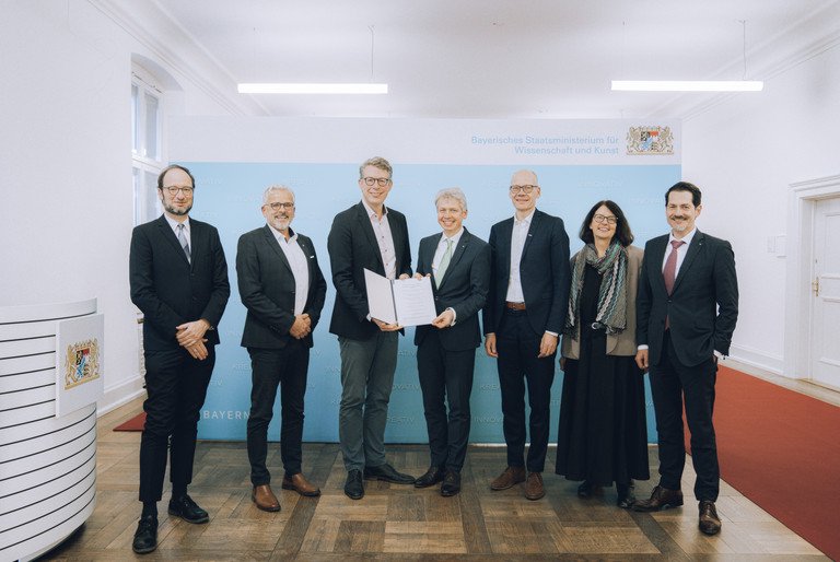 Sechs Herren und eine Dame &uuml;berreichen eine Kooperationsvereinbarung zur Gr&uuml;ndung des Zentrums Hochschule und Nachhaltigkeit Bayern (BayZeN) im Bayerischen Staatsministerium f&uuml;r Wissenschaft und Kunst: von links nach rechts sieht man Prof. Dr. Harald Kosch von der Universit&auml;t Passau, Dr. Eric Veulliet von der HSWT, Wissenschaftsminister Markus Blume, Prof. Dr. Clemens Bulitta von der OTHAW, Prof. Dr. Niels Oberbeck von der Ohm, Prof. Dr. Gabriele Gien von der KU, Prof. Thomas F. Hofmann von der TUM
