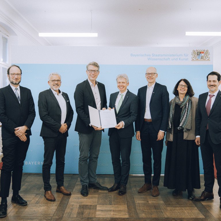 Sechs Herren und eine Dame &uuml;berreichen eine Kooperationsvereinbarung zur Gr&uuml;ndung des Zentrums Hochschule und Nachhaltigkeit Bayern (BayZeN) im Bayerischen Staatsministerium f&uuml;r Wissenschaft und Kunst: von links nach rechts sieht man Prof. Dr. Harald Kosch von der Universit&auml;t Passau, Dr. Eric Veulliet von der HSWT, Wissenschaftsminister Markus Blume, Prof. Dr. Clemens Bulitta von der OTHAW, Prof. Dr. Niels Oberbeck von der Ohm, Prof. Dr. Gabriele Gien von der KU, Prof. Thomas F. Hofmann von der TUM