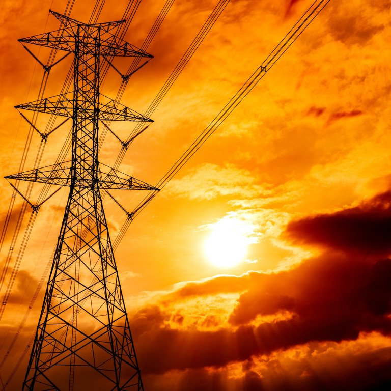 Eine Hochspannungsleitung auf einem Feld vor einem goldgelben wolkenbehangenen Himmel.