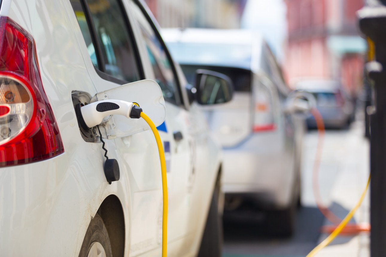 A white electric car hangs from a charging station for refueling. 