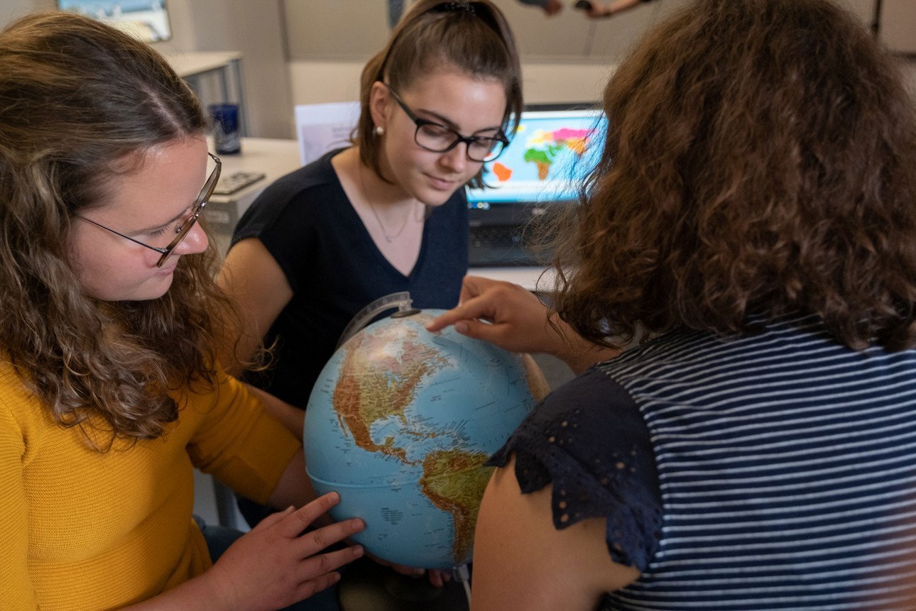 Drei Studentinnen sitzen um einen Globus und sehen sich die geographischen Grenzen Europas an