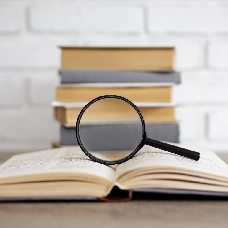 [Translate to English:] Symbolbild: Forschungsvorhaben unter ethischer Lupe. Eine Lupe steht auf einem aufgeschlagenen Buch und einem weiteren B&uuml;cherturm.