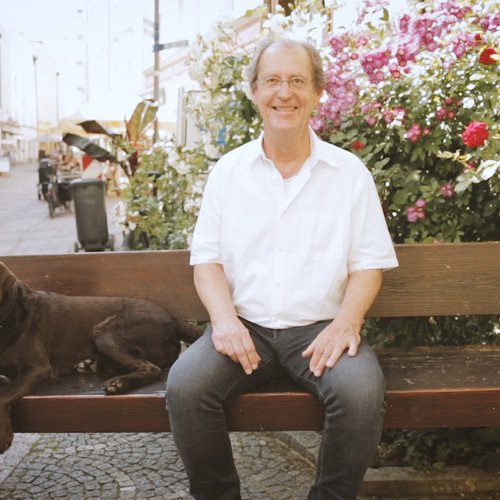 Prof. Dr. Herrmann de Meer sitzt auf einer Bank in der Passauer Innenstadt, neben ihm ein brauner Hund.