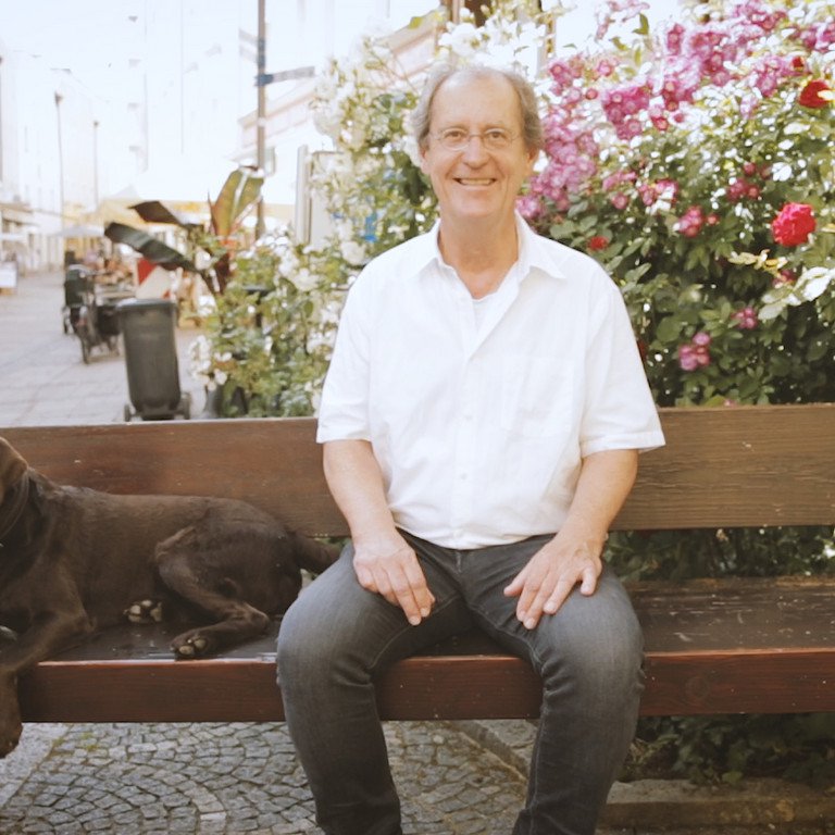Prof. Dr. Herrmann de Meer sitzt auf einer Bank in der Passauer Innenstadt, neben ihm ein brauner Hund.