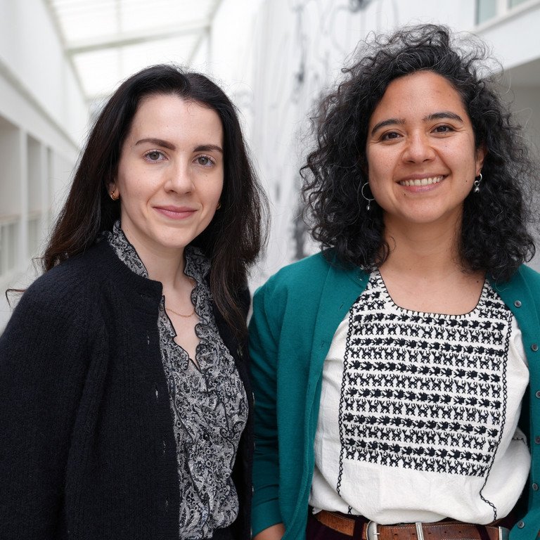 Dr. Pia Guti&eacute;rrez und Raquel Fern&aacute;ndez Men&eacute;ndez, zwei junge Frauen, stehen auf den G&auml;ngen der Universit&auml;t und l&auml;cheln freundlich.