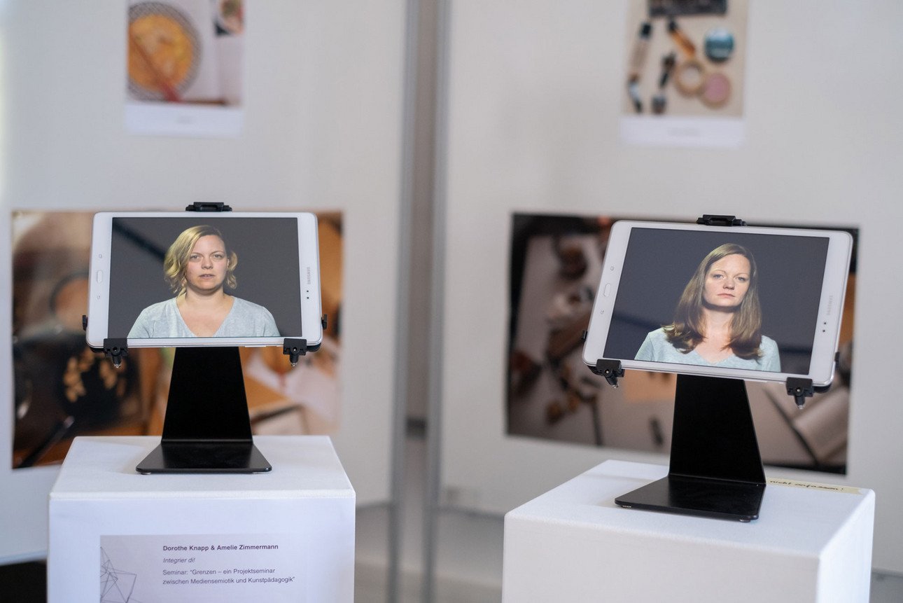 Foto von einer Videoinstallation mit zwei Tablets. Auf dem linken Tablet ist die Dozentin Dorothe Knapp und auf dem rechten die Dozentin Amelie Zimmermann zu sehen. 